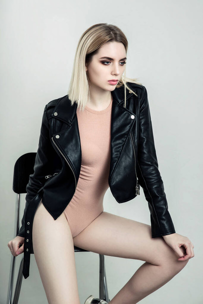 Fashion portrait of a beautiful girl model in leather jacket sits on chair. - Φωτογραφία, εικόνα