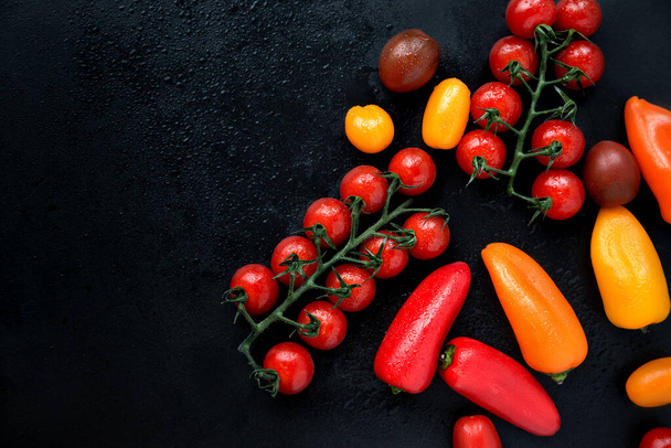 Tomatoes, cherry tomatoes and peppers on black background. Healthy eating and vegetarian food, cooking concept. Low key, selective focus. Top view, flat lay, copy space. - Fotoğraf, Görsel
