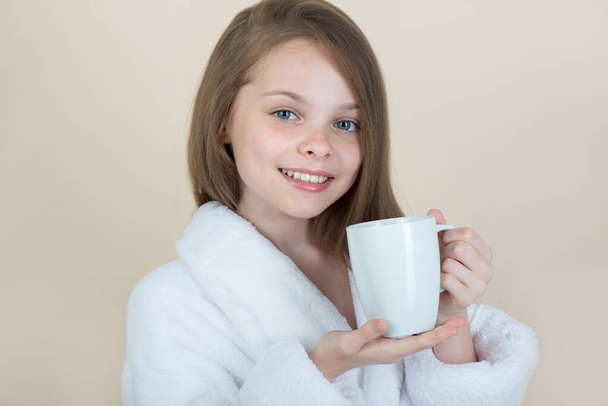 Little girl with white cup. Kid in bathrobe pointing to a clean mug. - Photo, Image