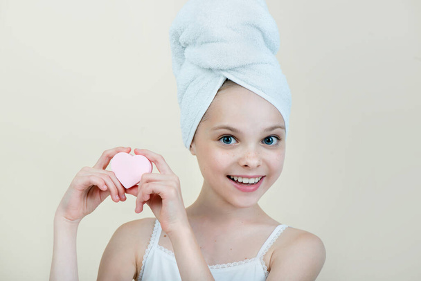 Pretty kid cleansing her face by heart shape cotton pad. Portrait of beautiful little girl enjoying skincare procedures. - Фото, изображение