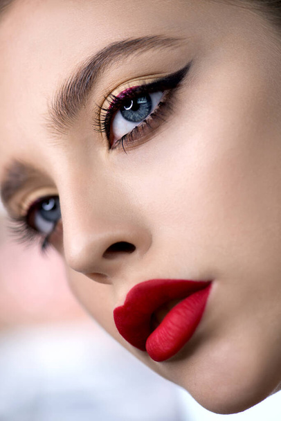 Portrait of beauty model with bright color red lip makeup and creative arrows on eyes. Beautiful young woman with professional make up  and long eyelashes Close up, Selective focus. - Foto, Bild