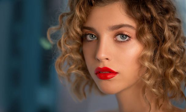 Portrait of Beautiful Fashion Model with Wavy Curly Hair and Colored Make-up with red Lips is posing front the Window. Make up and Hair. Haircare concept. Close-up, Selective focus. - Photo, Image