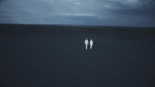 Kaksi ihmistä valkoisissa suojapuvuissa kävelee kivikentällä yöllä. - Materiaali, video