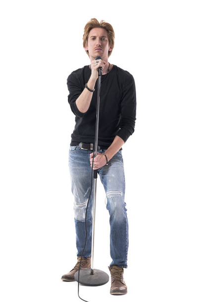 Fajny macho stylowy piosenkarz rocker trzymając mikrofon na stoisku. Długość całego ciała odizolowana na białym tle. - Zdjęcie, obraz