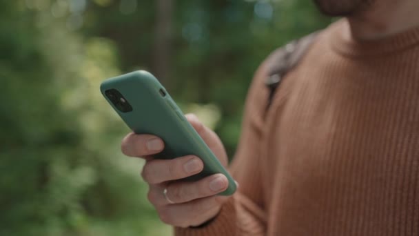 Primer plano de un teléfono móvil en manos de un viajero masculino caminando por el bosque. Redes sociales Navegador y mensajero. Utilice su teléfono móvil para dar un paseo por el bosque - Imágenes, Vídeo