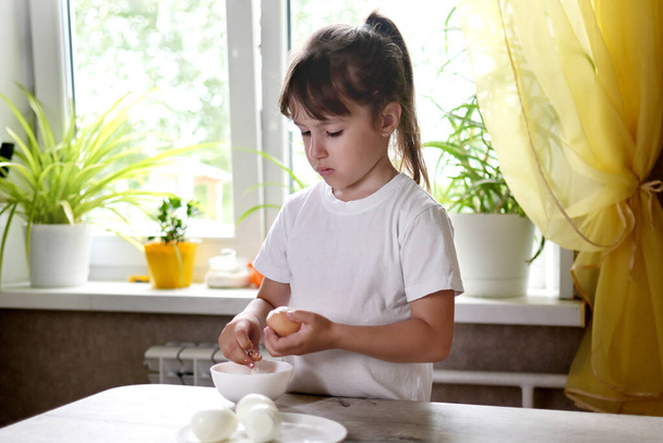 styl życia przedszkolak dziewczynka gotować jedzenie w kuchni. rozwój umiejętności motorycznych w codziennym życiu z materiałów złomowych. dziecko czyści jajka - Zdjęcie, obraz