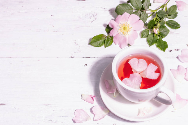 Tee aus Hagebuttenblüten. Sommerlicher Vitamindrink, hartes Licht, dunkler Schatten. Weißer Holzhintergrund, Kopierraum - Foto, Bild