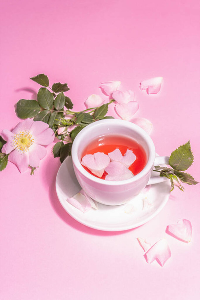 バラの腰の花からお茶。夏のビタミンドリンク、ハードライト、暗い影。ピンクのパステル背景、コピースペース - 写真・画像