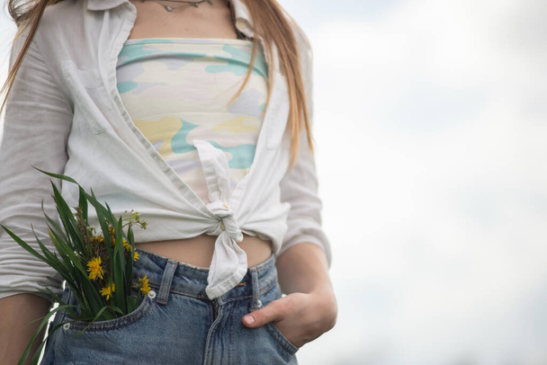 spring in your pocket. A bouquet of wildflowers sticking out of the jeans pocket of a teenage girl. - Foto, imagen