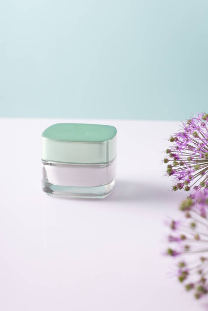 Schönheit kosmetische Creme in einem weißen Behälter, mit Blumen auf einem weiß-blauen Hintergrund. - Foto, Bild