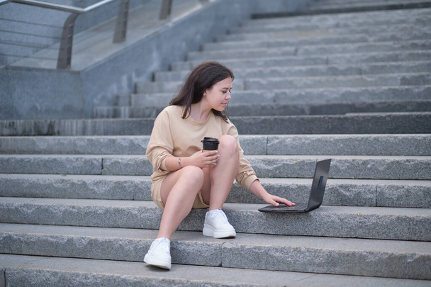 молодий студент сидить на сходах поза офісною будівлею в кампусі, працює на ноутбуці, читає. іспаномовна жінка використовує свій ноутбук. Технологія та концепція способу життя
 - Фото, зображення