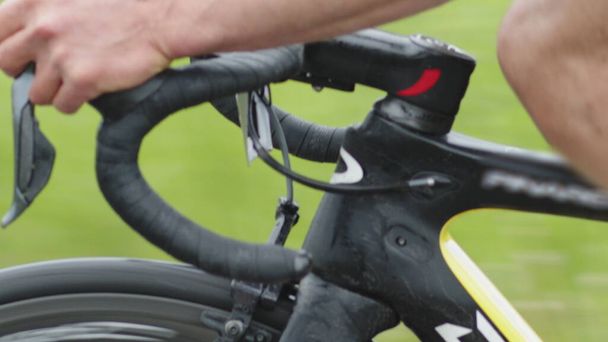 Close-up van het gebogen stuurwiel van een racefiets, de handen van een fietser schakelen snelheid tijdens het rijden op de weg. - Foto, afbeelding