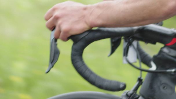 Nahaufnahme des gebogenen Lenkrads eines Rennrads, die Hände eines Radfahrers, der während der Fahrt die Geschwindigkeit wechselt. - Foto, Bild