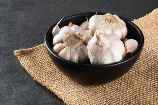 Garlic Cloves and Bulb in black bowl on jute and dark background. - Foto, immagini