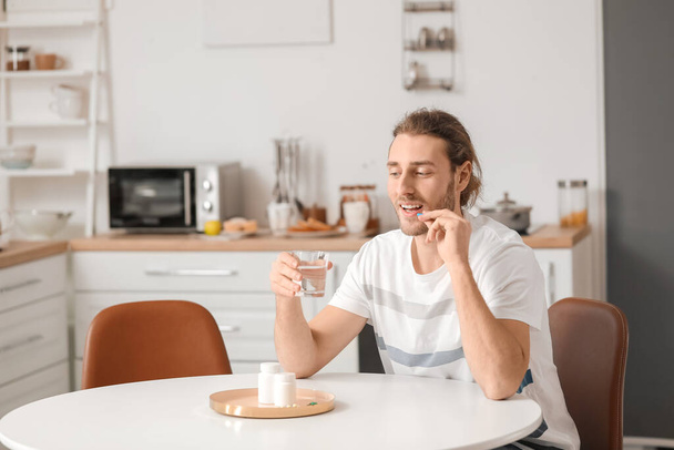 Handsome young man taking pills in kitchen - 写真・画像