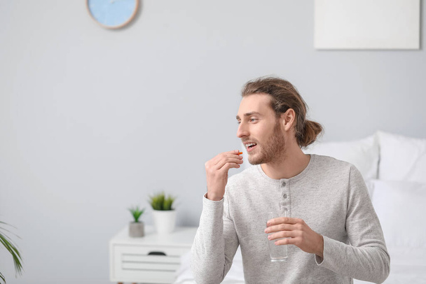 Handsome young man taking pills in bedroom - Photo, Image