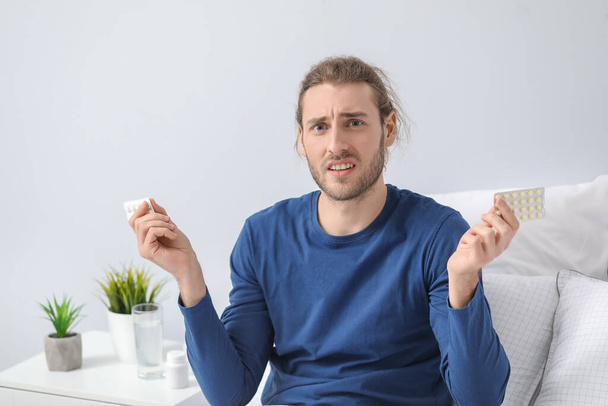 Displeased young man with pills at home - Photo, Image