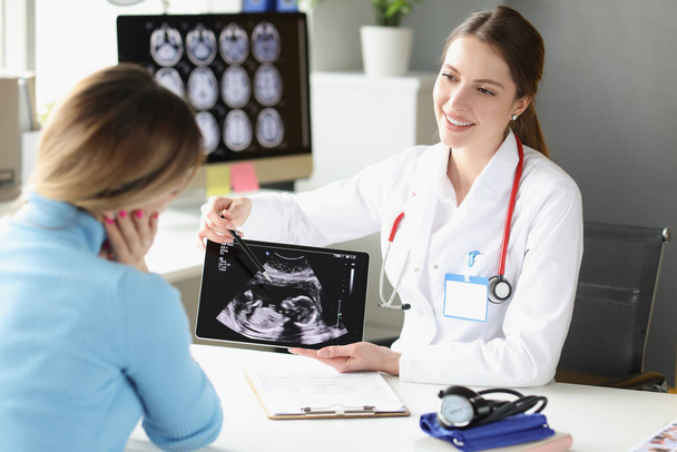 Woman obstetrician gynecologist showing patient photograph of ultrasound examination of fetus on digital tablet - Photo, image