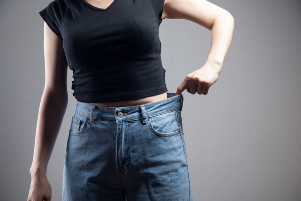 junges Mädchen zieht Jeans auf grauem Hintergrund - Foto, Bild