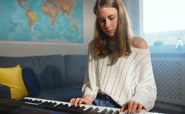 Εφηβική κοπέλα που παίζει ηλεκτρονικό μουσικό όργανο στο σπίτι. - Φωτογραφία, εικόνα
