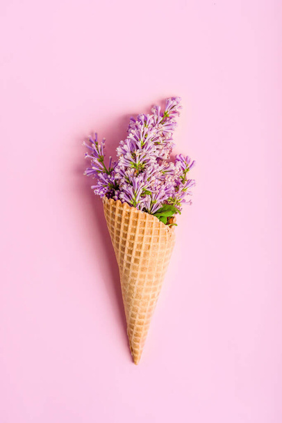 Un ramo de lilas en un cono de gofre sobre un fondo rosa. Vista superior del fondo floral. - Foto, imagen
