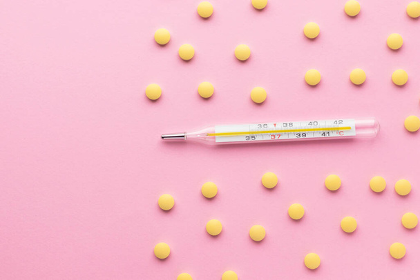 Mercury thermometer and yellow pills isolated on pink background. Epidemic, painkillers, healthcare and treatment concept. Flat lay. Top view with copy space. - Photo, Image