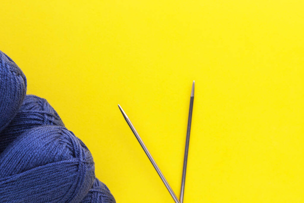 Breigarens van klassieke blauwe denim kleur en metalen naalden op gele achtergrond. Ballen van wol draden. Handgemaakt en hobby concept. Vlakke lay, bovenaanzicht met kopieerruimte. - Foto, afbeelding