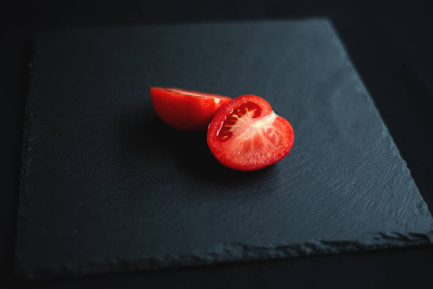 group of tomatoes, one cut in half, rests on a black board for serving - Foto, Imagen