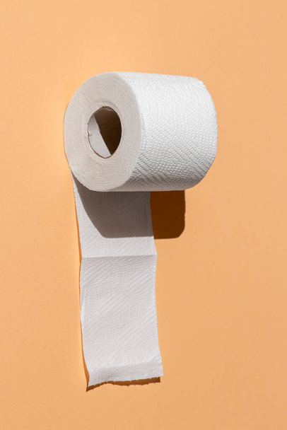 roll of a perforated toilet paper isolated on a sand color background close-up. hard shadows from the sun at noon - Фото, изображение