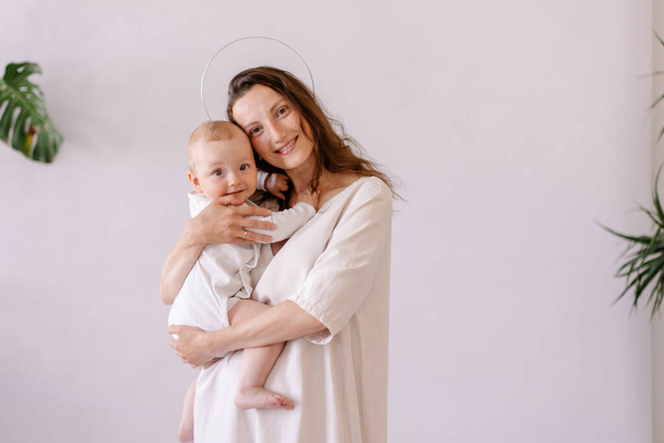 mother in white clothes holds a baby in her arms. Purity innocence sanctity of motherhood. image of madonna. Mom and child. happiness of motherhood. Eco parenting vegan. Closeness to nature. Childhood - Photo, Image
