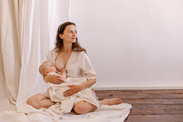 mother is breastfeeding her baby. Woman in white and child on her arms. Kid sucks breast milk. Holy motherhood. Caring tenderness protection. Mother love concept.  Natural nutrition. Eco parenting - Zdjęcie, obraz