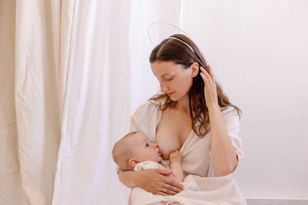 mother is breastfeeding her baby. Woman in white and child on her arms. Kid sucks breast milk. Holy motherhood. Caring tenderness protection. Mother love concept.  Natural nutrition. Eco parenting - Foto, Imagen
