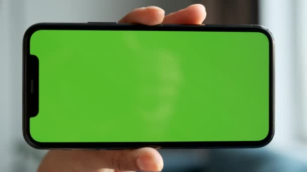 крупным планом женской руки, держащей горизонтально смартфон с зеленым экраном, хромакей для использования новых технологий, социальных сетей, видео, фильмов и фотографий - Кадры, видео