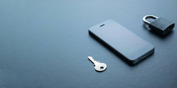 Sicurezza mobile. Moderno telefono cellulare grigio spazio con lucchetto, chiave su sfondo scuro. Furto di identità e concetto di sicurezza informatica - Foto, immagini