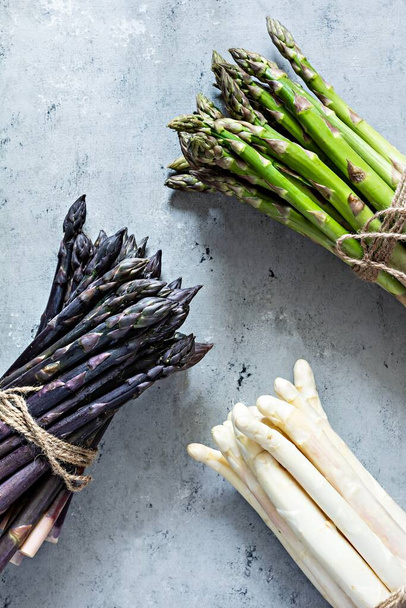 Raw white, purple, green asparagus on a blue background. Raw food concept. - Photo, Image