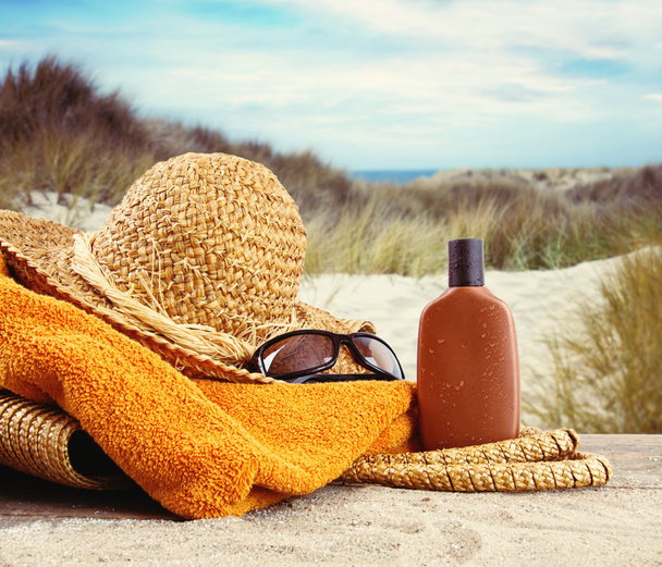 stro hoed met handdoek en lotion op het strand  - Foto, afbeelding