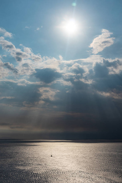 Promienie słońca świecą choć chmury nad morzem w Grecji. Dramatyczna chmura na śródziemnomorskiej powierzchni wody morskiej. Pionowe - Zdjęcie, obraz