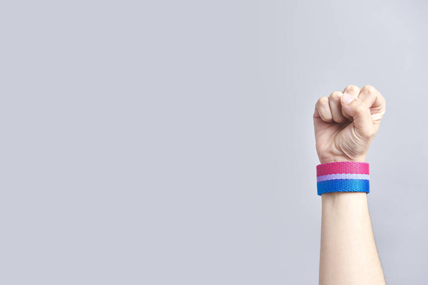 Poing levé d'un jeune homme portant un bracelet aux couleurs du drapeau bisexuel. Concepts de lutte pour l'égalité des droits, la non-discrimination et le respect de la diversité sexuelle. Image avec espace de copie. - Photo, image
