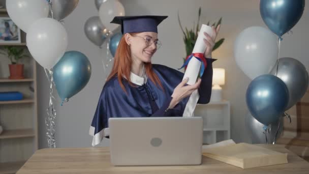 online graduation, beautiful female student in academic gown rejoices diploma during virtual congratulation ceremony for graduates via video link on laptop during distant education - Footage, Video
