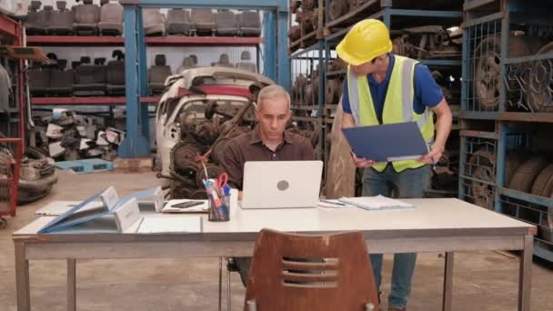 Двое мужчин на складе запасных частей для автомобилей: кавказский владелец использует ноутбуки для проверки заказов, в то время как азиатские мужчины осматривают многочисленные запасные части двигателей, собранные в автомобильной промышленности. - Кадры, видео