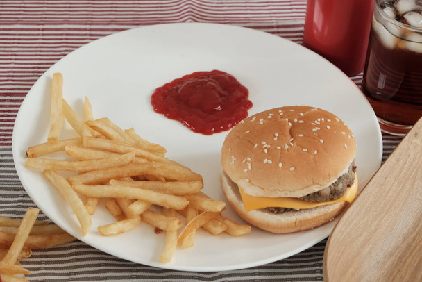 Detailní záběr: kečup nalitý do bílého prázdného talíře umístěného na ubrusu. Jíst s nezdravým jídlem umístěným vedle něj, jako jsou hranolky, hamburgery a cola, což jsou nezdravé fast foods. - Fotografie, Obrázek