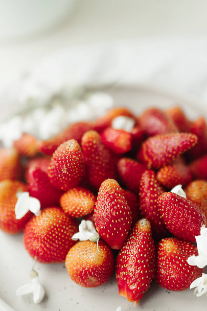 皿の上の新鮮なイチゴと装飾として小さな白い花。健康食品だ。生の食事よ。食べ物の内容だ。旬のベリー。選択的焦点 - 写真・画像