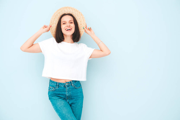 Portrait of young beautiful smiling female in trendy summer hipster  clothes. Sexy carefree woman posing near blue wall in studio. Positive model having fun in hat. Cheerful and happy - Φωτογραφία, εικόνα