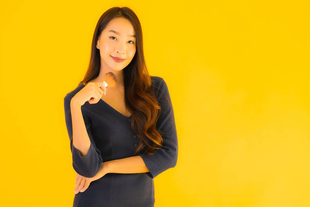 Portrait belle jeune femme asiatique avec pinceau de maquillage sur fond jaune isolé - Photo, image