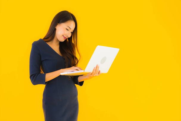 Retrato hermosa joven asiática mujer con portátil o computadora en amarillo aislado fondo
 - Foto, Imagen
