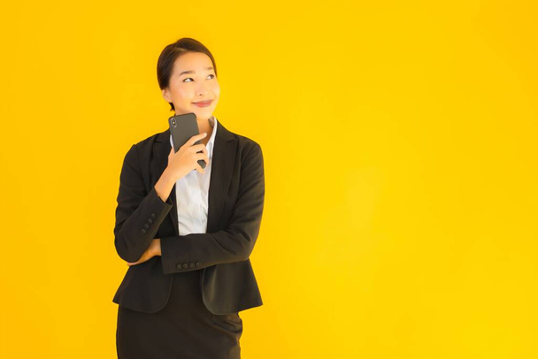 Портрет красивый молодой бизнес азиатской женщины со смартфоном и кофейной чашкой на желтом изолированном фоне
 - Фото, изображение