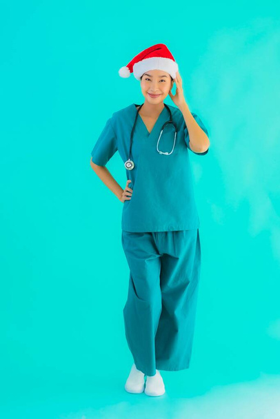 Portré gyönyörű fiatal ázsiai orvos nő visel karácsonyi kalap mosollyal boldog kék elszigetelt háttér - Fotó, kép