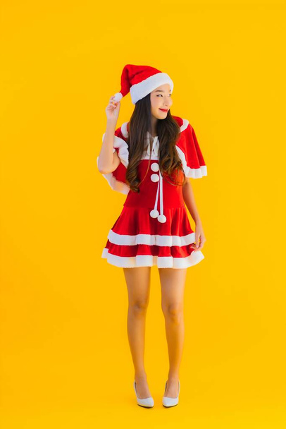 Porträt schöne junge asiatische Frau Weihnachten Kleidung und Hut Lächeln glücklich mit anderen Maßnahmen auf gelbem Hintergrund isoliert - Foto, Bild