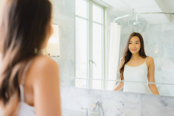 Портрет красивая молодая азиатская женщина проверить и макияж ее лицо на зеркале в ванной комнате интерьера
 - Фото, изображение