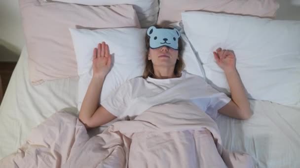 Boldog álmos fiatal felnőtt nő ébred fekve fehér ágyban - Felvétel, videó